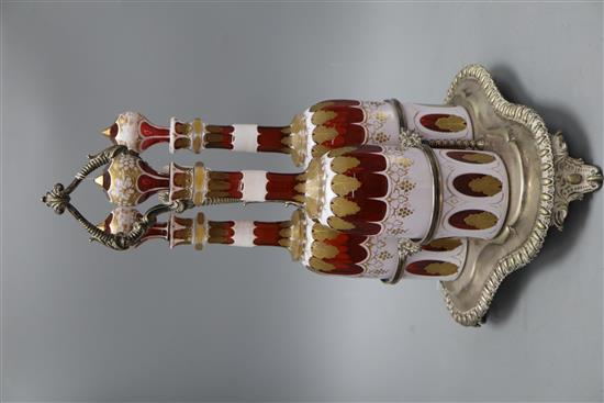 A plated three bottle tantalus, the decanters overlaid glass with gilt decoration, height 37cm
